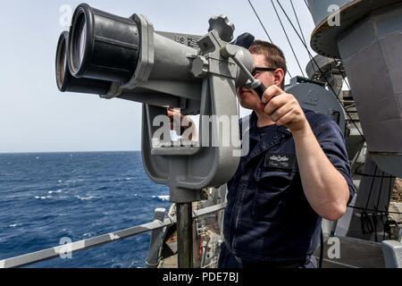 U.S. 5TH FLEET AREA OF OPERATIONS (May 9, 2018) Electronic's Technician 3rd Class Patrick Turpin looks through binoculars for contacts of interests on the bridge wing of the Arleigh Burke-class guided-missile destroyer USS Laboon (DDG 58). Laboon is deployed to the U.S. 5th Fleet area of operations in support of maritime security operations to reassure allies and partners and preserve the freedom of navigation and the free flow of commerce in the region. Stock Photo