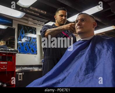 WATERS SOUTH OF JAPAN (May 16, 2018) Machinist’s Mate (Nuclear) 2nd Class Patrick Rivera, from Grant, New Mexico, gives Chief Machinist’s Mate (Nuclear) Sean Glen, from Dallas, a haircut in the barbershop aboard the Navy’s forward-deployed aircraft carrier, USS Ronald Reagan (CVN 76). Ronald Reagan, the flagship of Carrier Strike Group 5, provides a combat-ready force that protects and defends the collective maritime interests of its allies and partners in the Indo-Asia-Pacific region. Stock Photo