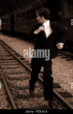 Young man in a suit running in an old narrow guage trainyard next to a train.  Exclusive, unique royalty free stock photos Stock Photo