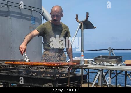 MEDITERRANEAN SEA (May 20, 2018) - U.S. Marine Corps Staff Sgt. Ryan Bartolo, a platoon sergeant, assigned to Fox Company, Battalion Landing Team, 2nd Battalion, 6th Marine Regiment, 26th Marine Expeditionary Unit (MEU) grills hot dogs during a Steel Beach event aboard the Harpers Ferry-class dock landing ship USS Oak Hill (LSD 51) while underway in the Mediterranean Sea, May 20, 2018. Oak Hill, home ported in Virginia Beach, Virginia, and the 26th MEU are conducting naval operations in the 6th Fleet area of operations. Stock Photo