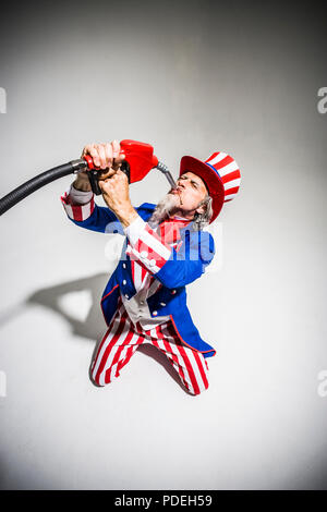 Uncle Sam sucking gasoline from a gas pump nozzle. Addicted to oil / fossil fuels. Stock Photo