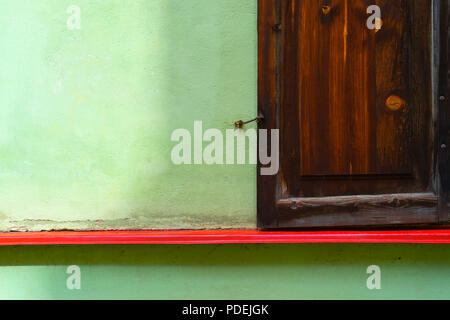 Wooden brown shutters with crochet on a green wall with a red sill line Stock Photo