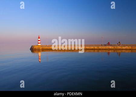 Lithuania. Nida. A couple of people riding bicycles on the breakwater into the sea to the lighthouse at sunset Stock Photo