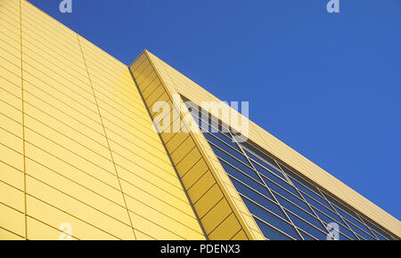 Modern building surface, diagonal and from below view in yellow and blue color with blue sky above Stock Photo