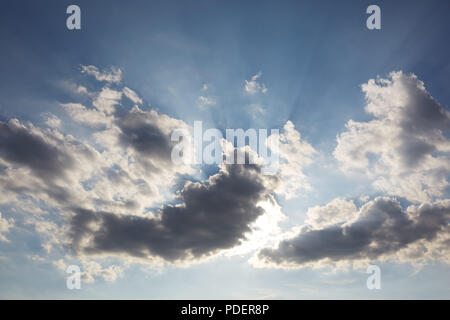 Looking up at a blue sky with rays of light shining from behind clouds like they are the heavens above Stock Photo