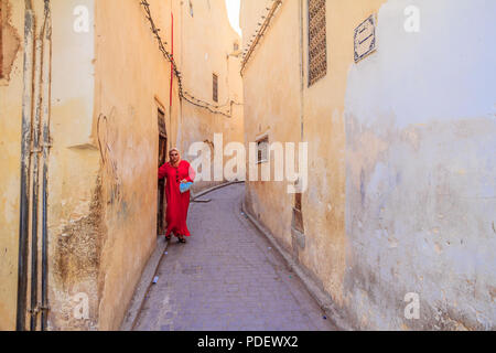 Fes, Morocco - May 11, 2013: Woman wearing a kaftan, traditional Moroccan clothing, stepping out into a narrow street in Fes Medina in Morocco Stock Photo