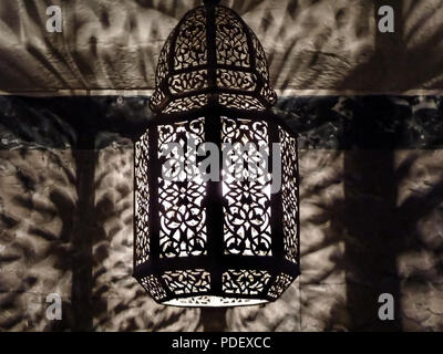 Moroccan Ornate Pierced Metal Filigree Lamp casting intricate shadows on the wall Stock Photo