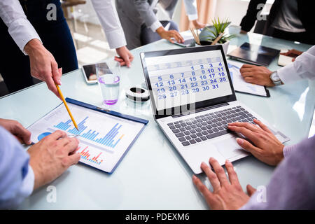 Businesspeople Using Calendar On Laptop While Analyzing Graphs Over Desk Stock Photo