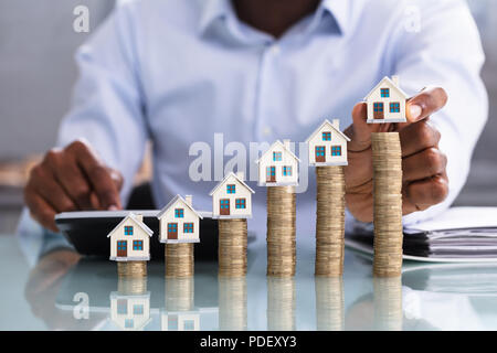 Close-up Of A Business Person Placing Miniature House Model On Stacked Coins