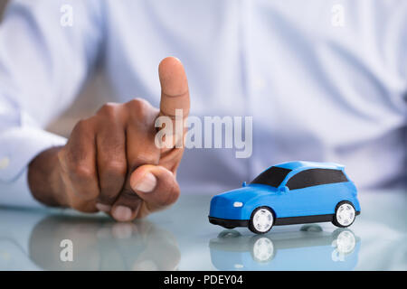 Close-up Of A Businessman Pointing Finger With Blue Toy Car On The Desk Stock Photo
