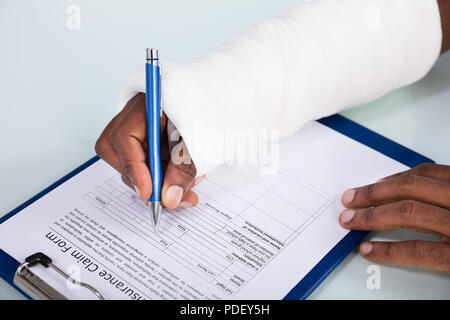 Overhead View Of Injured Man With Bandage Hand Filling Insurance Claim Form On Clipboard Stock Photo