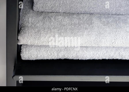 Grey and black towels are on the shelf in the bathroom. Towels hung on hooks. Bath accessories. Stock Photo