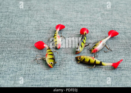 Silicone bait. Twisters on the background of burlap. Lures with triple hooks in the form of a small perch. Red tail. Stock Photo
