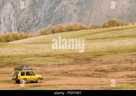 Yellow SUV Car On Off Road In Spring Mountains Landscape. Drive And Travel Concept. Landscape Of Gorge At Spring Season. Stock Photo