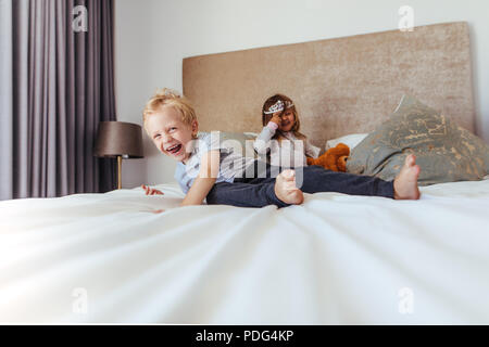 Happy kids playing in bedroom. Little boy smiling with girl at the back in crown on the bed. Stock Photo