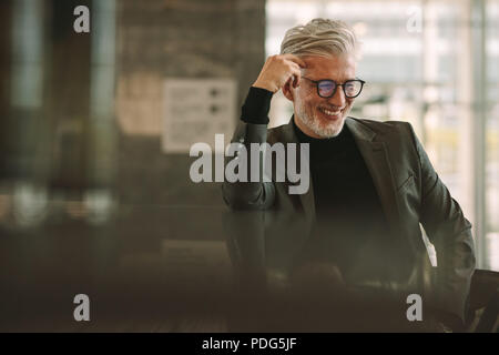 Smiling mature businessman sitting at coffee shop. Senior man in formal wear relaxing at cafe. Stock Photo