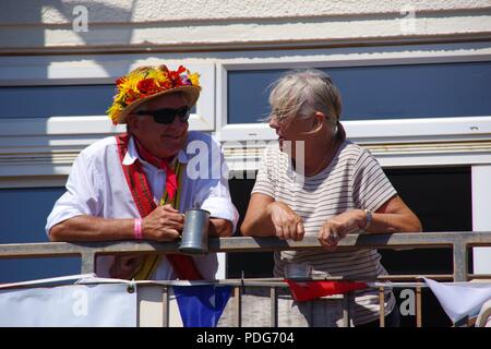 Pair of Elderly Morris Dancers Drinking from Pewter Pint with a Flowery Straw Hat on a Balcony. Sidmouth Folk Festival. East Devon, UK. Stock Photo