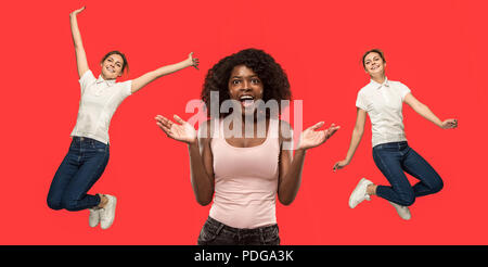 Wow. Beautiful female portrait isolated on red studio backgroud. Young surprised women holding hands by head, looking at camera. Girl jumping. Human emotions, facial expression concept. Trendy colors Stock Photo