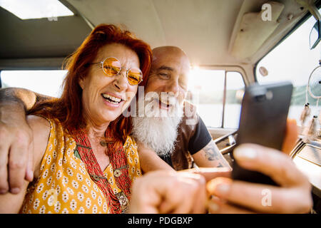 Old hipster couple using a smartphone inside their vintage van  Stock Photo