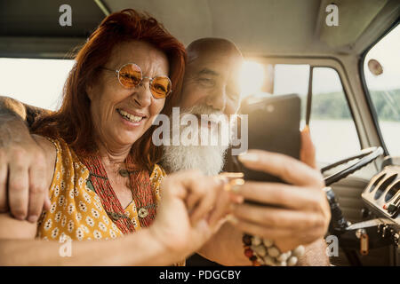 Old hipster couple using a smartphone inside their vintage van  Stock Photo