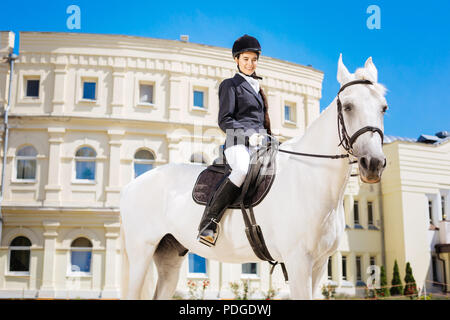 Elegant gentle woman riding her white horse on big race track Stock Photo