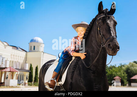 Cute cowboy girl hugging her beautiful black horse Stock Photo