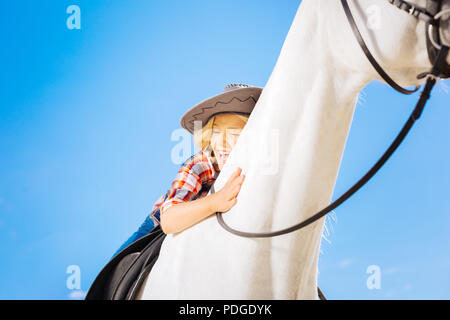 Blonde-haired funny girl laughing while riding her white horse Stock Photo