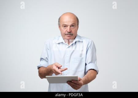 Mature european man using a digital tablet. He is puzzled and confused. He did not know how to use his new gadget Stock Photo
