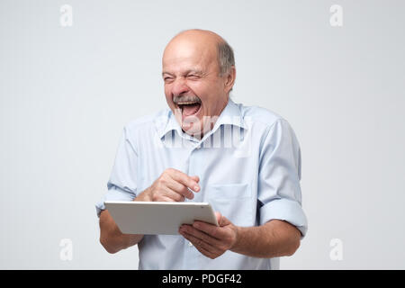 Cheerful mature european man laughing holding tablet over white background. Stock Photo
