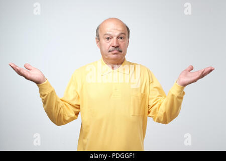 Emotional senior man not sure for something. Studio shot, gray background Stock Photo