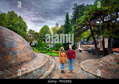 Tourist woman in brown jacket and man in red shirt standing near the dome of Public Sulfuric bath district in central Tbilisi, Georgia Stock Photo