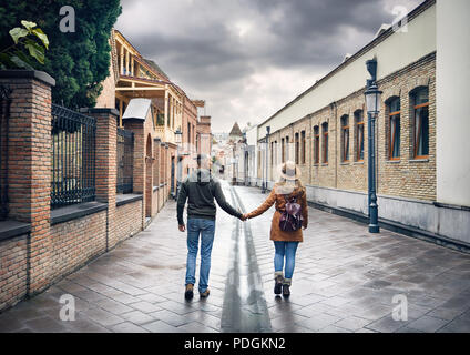 Tourist woman in brown hat and man in red shirt walking down old the Old streets of central Tbilisi, Georgia Stock Photo