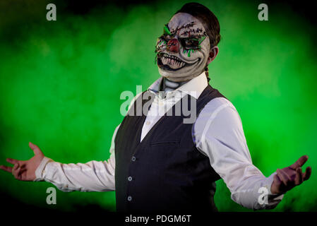 Portrait of a nicely dressed man wearing an evil clown mask with stitches and skull makeup underneath. Horror and Halloween themed, shot with theatric Stock Photo