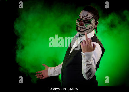 Portrait of a nicely dressed man wearing an evil clown mask with stitches and skull makeup underneath. Horror and Halloween themed, shot with theatric Stock Photo