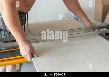 The man is cutting the floor tiles using a tile cutter machine. Stock Photo