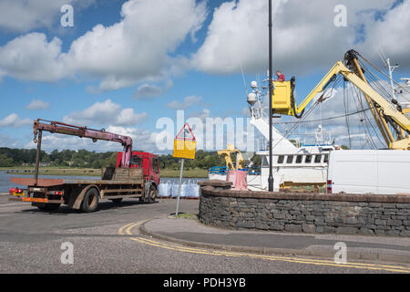 A view of Kirkcudbright Harbour which shows a lorry preparing to load a catch of shellfish which has just been unloaded from from a fishing boat. Stock Photo