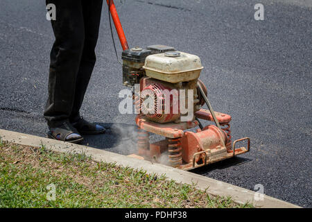 Worker uses vibratory plate compactor compacting asphalt at road repair Stock Photo
