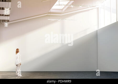 Woman walking near blank white wall mockup in modern gallery with sunset. Girl admires a clear big stand mock up in museum with contemporary art exhibitions. Large hall interior, sunrise from windows Stock Photo