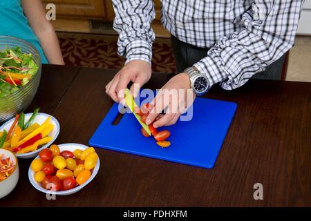 Man slicing tomatoes with a nice on a blue cutting board in a home kitchen Stock Photo