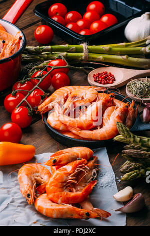 Top view of rustic wooden table full of prawns and some ingredients for seasoning and vegetables to mix them Stock Photo