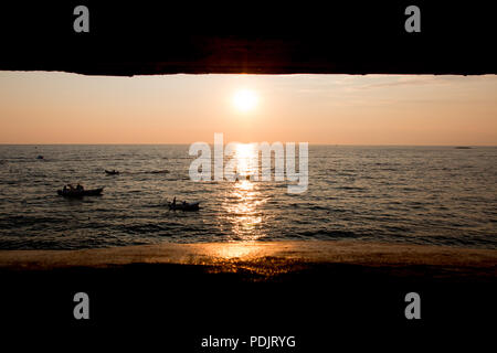 Rovinj, Croatia - July 24, 2018: View from an old bunker on the shore of the port city of Rovinj to a sunset with fishing boats. Stock Photo