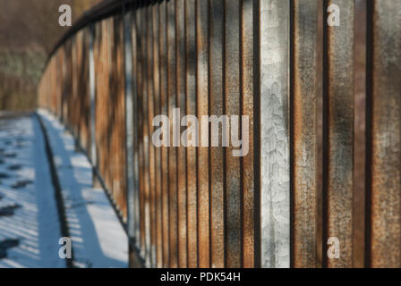 Metal, rusty bridge railing covered in snow lit by morning sun Stock Photo