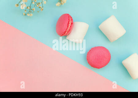 Top view of mini pink macaron or macaroon french desserts cake with marshmallows on soft sweet pink and blue pastel geometric paper flat lay backgroun Stock Photo