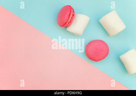 Top view of mini pink macaron or macaroon french desserts cake with marshmallows on soft sweet pink and blue pastel geometric paper flat lay backgroun Stock Photo