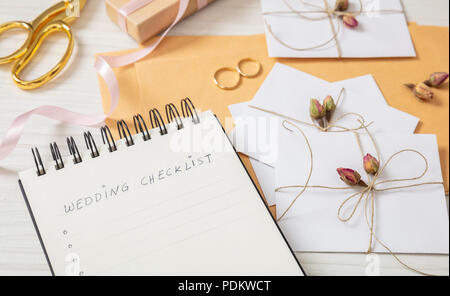 Wedding preparation.Flat lay and close up view of checklist and wedding invitations on a white wooden tabletop, blank space. Stock Photo