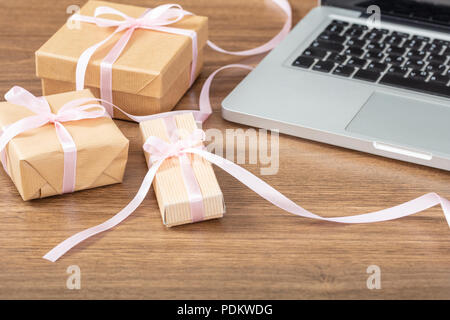 Presents concept. Close up of beige craft gift boxes and computer on a wooden background. Stock Photo