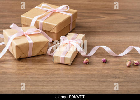 Presents concept. Close up of beige craft gift boxes with pink silky ribbon on a wooden background, copy space. Stock Photo
