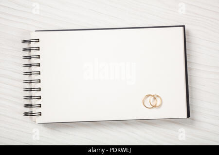 Love and marriage concept.  Golden wedding rings on a blank notebook, top view, isolated and copy space, on a white wooden background. Stock Photo