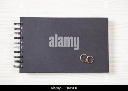 Love and marriage concept.  Golden wedding rings on a black notebook, top view, isolated and copy space, on a white wooden background. Stock Photo