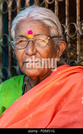 Nilavagilukaval, Karnataka, India - November 1, 2013: Closeup of graying grandmother with circular glasses, golden jewelry and bright red, green sari. Stock Photo